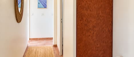 A hallway with a woven rug, a wooden door, and a framed picture on the wall.