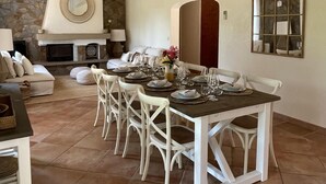 Comedor con chimenea de piedra, sillas blancas y una mesa de comedor preparada para seis comensales.