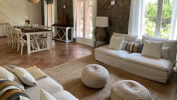Amplia sala de estar con pared de piedra, un sofá blanco y una mesa de comedor preparada para cuatro comensales.