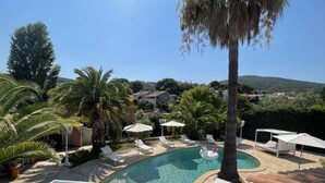 Una piscina con sillas de descanso y sombrillas, rodeada de palmeras y vista a una colina.