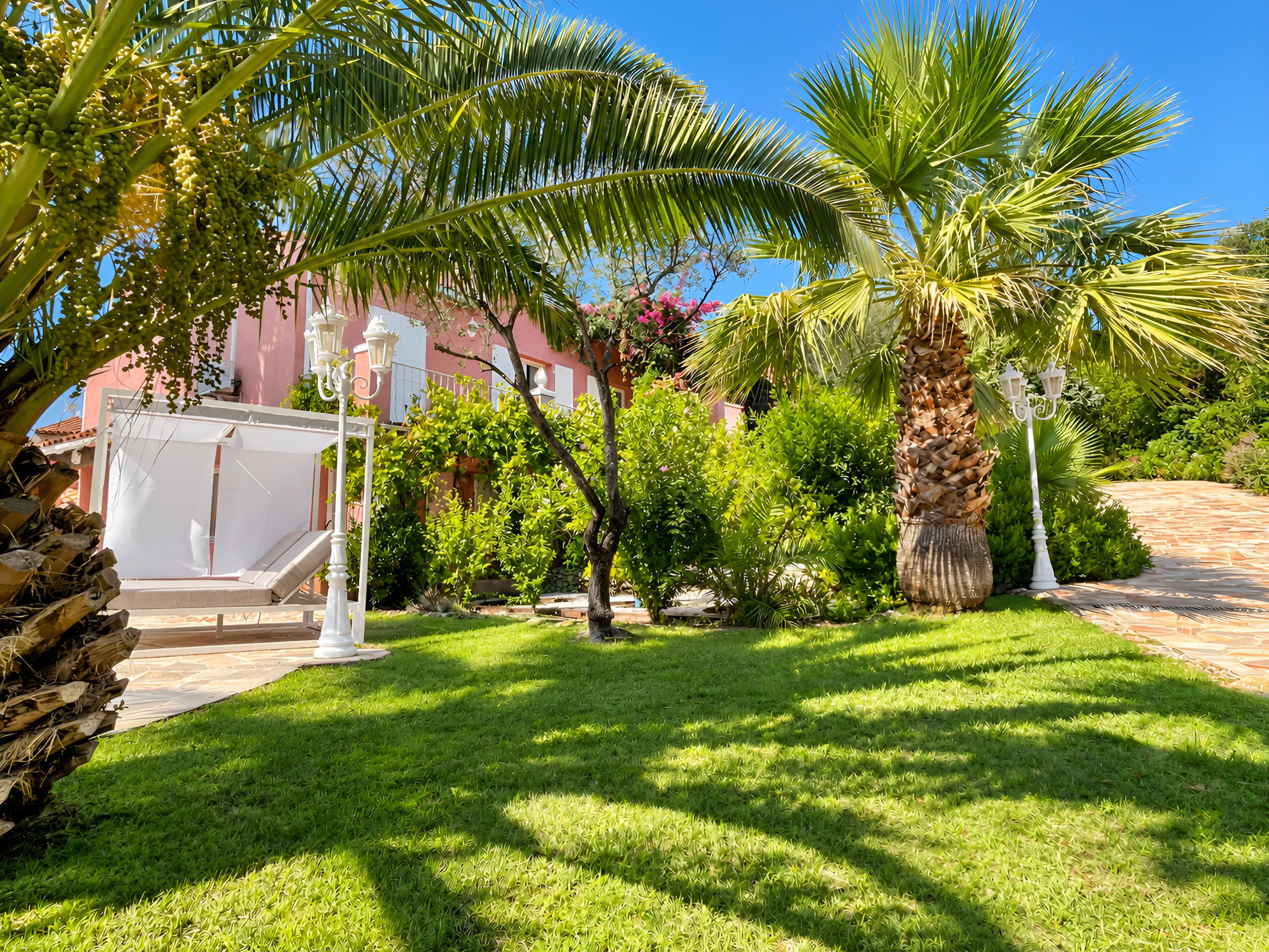 A well-maintained garden with palm trees, a white gazebo, and a paved walkway.