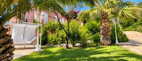 A well-maintained garden with palm trees, a white gazebo, and a paved walkway.
