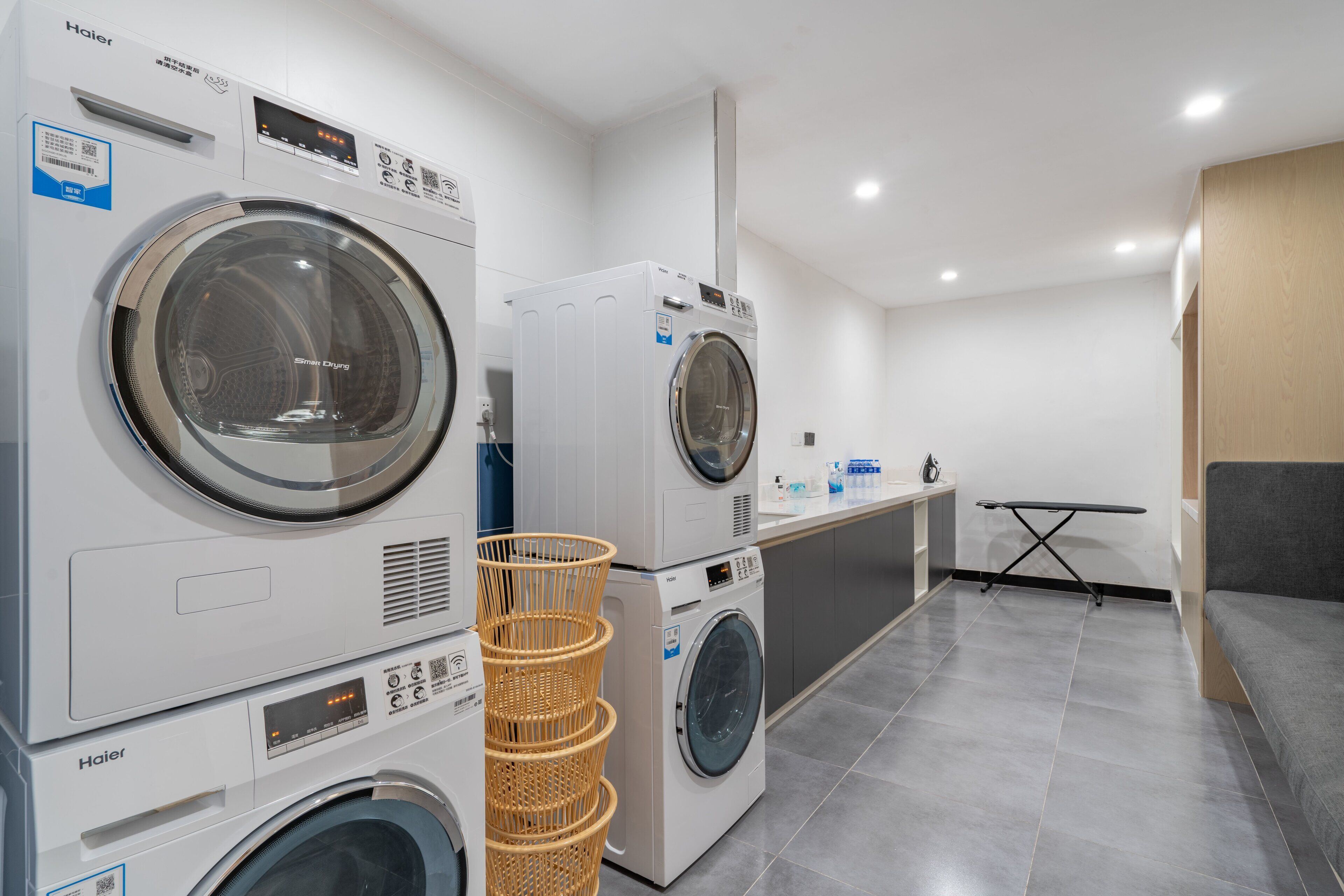 A laundry facility with multiple Haier washing machines, a drying rack, and a ironing station.