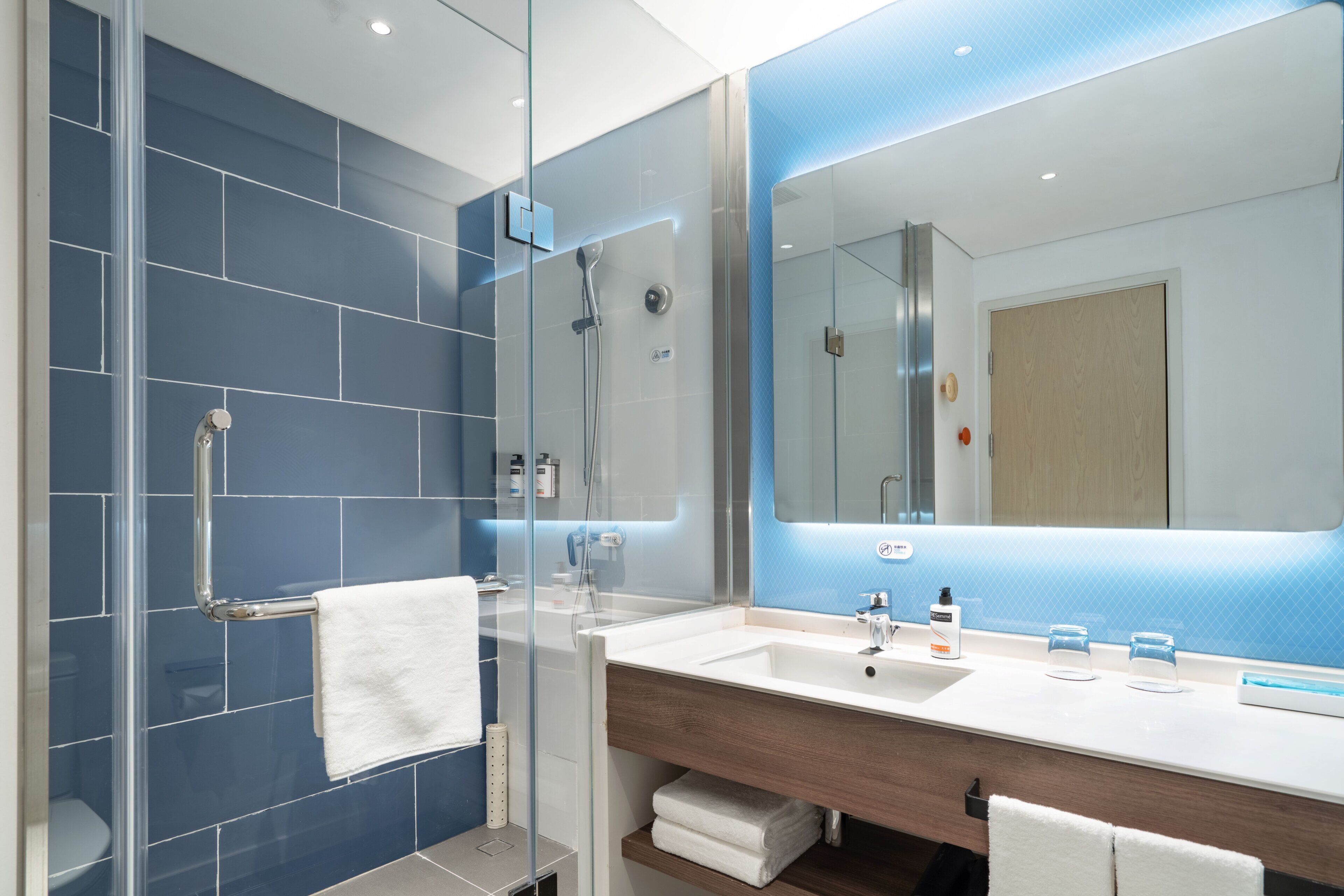 A modern bathroom with a glass-enclosed shower, a large mirror, and a vanity with a wooden countertop.
