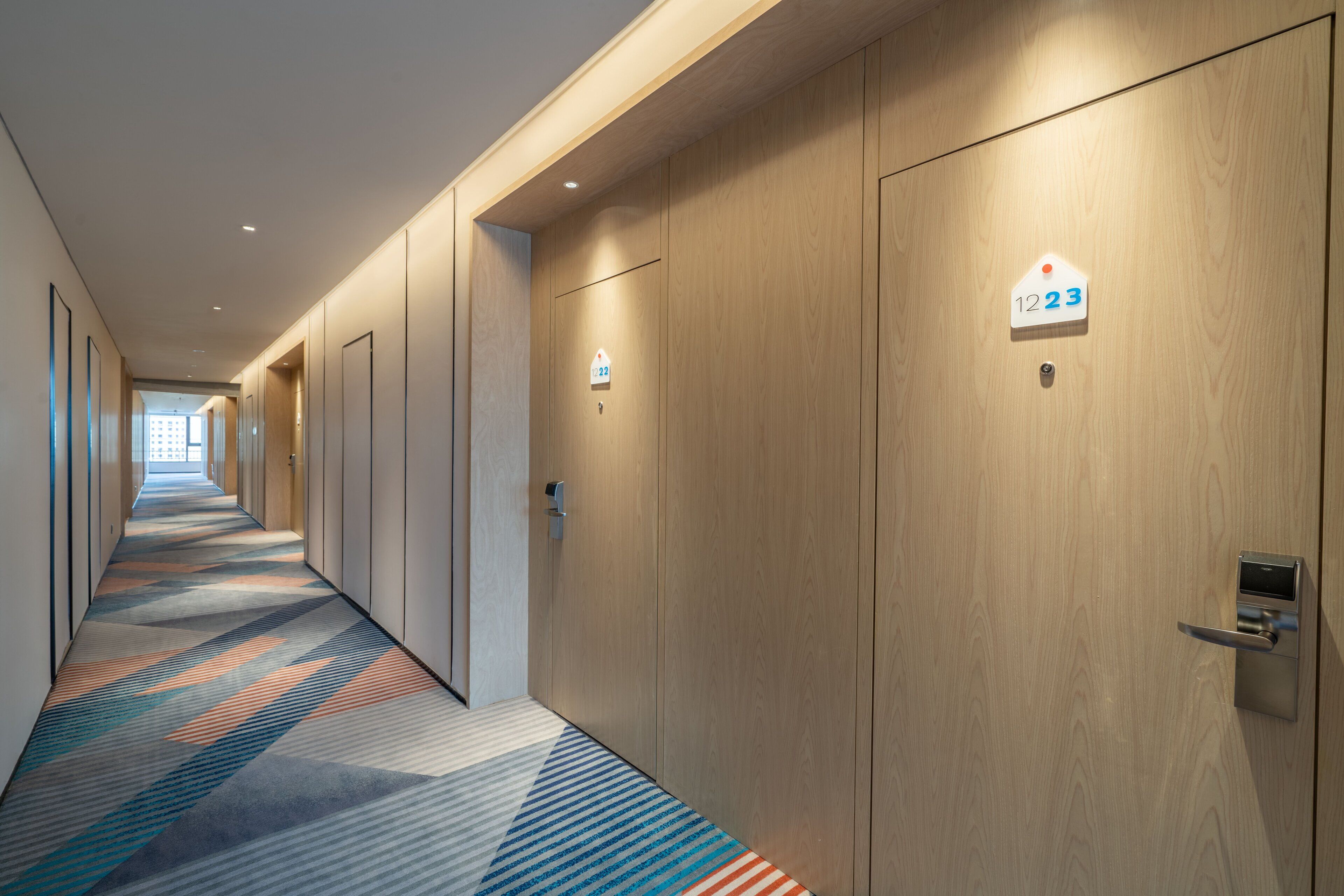 A hotel corridor with wooden doors, numbered room signs, and a patterned carpet.