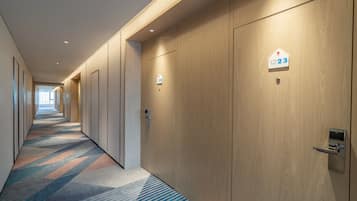 A hotel corridor with wooden doors, numbered room signs, and a patterned carpet.