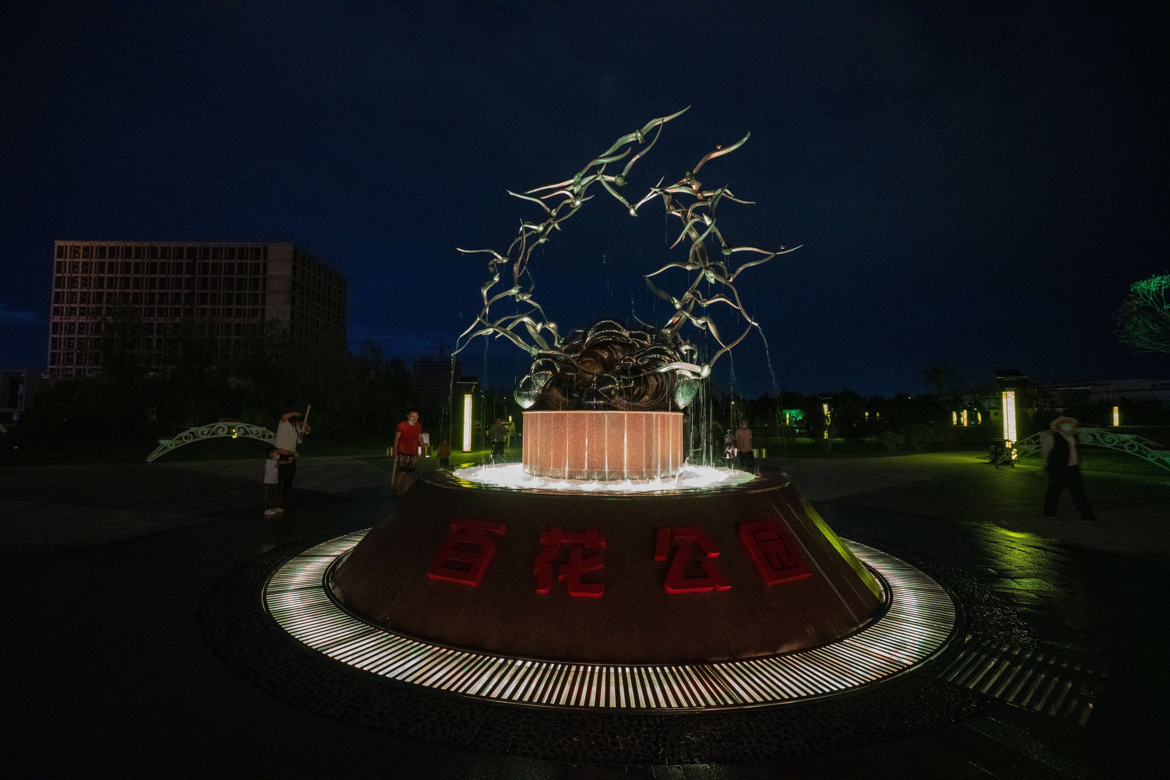 A nighttime sculpture with a circular base and red text, surrounded by a paved area.
