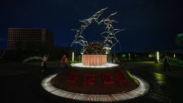 A nighttime sculpture with a circular base and red text, surrounded by a paved area.