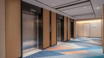 A modern elevator area with metallic elevator doors, a patterned carpet, and a plain wall with a door at the end.