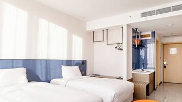 Habitación de hotel con dos camas, un escritorio con silla, un baño con lavamanos y una puerta que da a otra habitación.