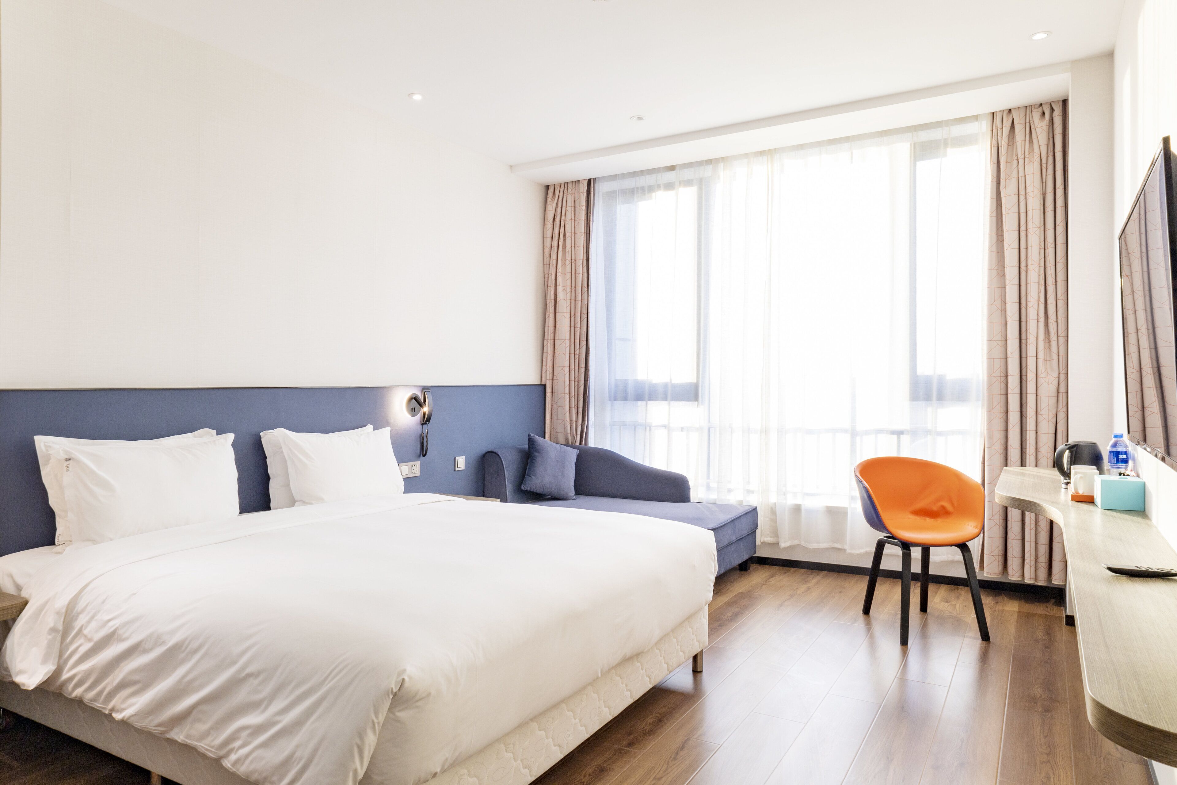 A hotel room with a large bed, a desk, a chair, and a window with curtains.