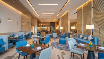 Un moderno vestíbulo de hotel con zonas de estar, mesas y un bar central.