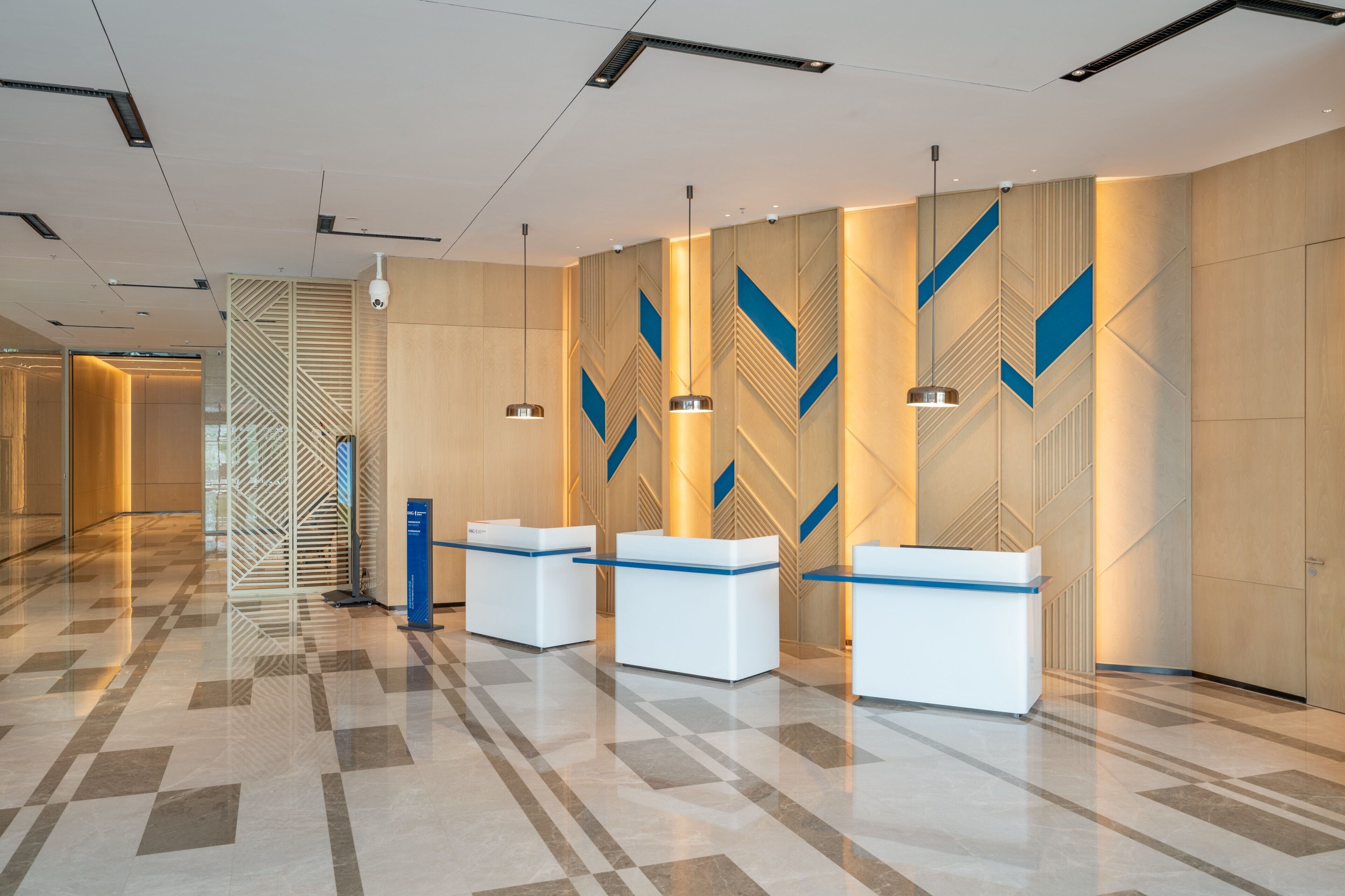A modern reception area with three white reception desks, a patterned wall, and a geometric floor design.