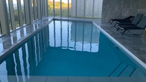 An indoor swimming pool with clear glass walls, a tiled floor, and a few lounge chairs. - Cottage with 2 bedrooms - unobstructed sea view (Plouha)
