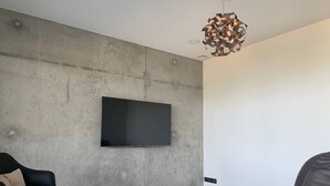 A modern living room with a flat-screen TV mounted on a textured wall, a black leather sofa, a white coffee table, and a unique pendant light. - Cottage with 2 bedrooms - unobstructed sea view (Plouha)