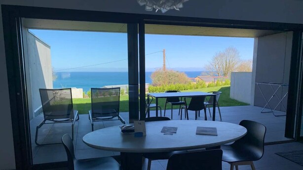 A modern dining area with a round table and chairs, large glass doors leading to a balcony with a view of the sea. - Cottage with 2 bedrooms - unobstructed sea view (Plouha)