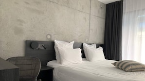 A modern hotel room with a large bed, a chair, a bedside table, and a concrete wall. - Cottage with 2 bedrooms - unobstructed sea view (Plouha)