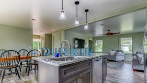 A modern kitchen with a central island, pendant lighting, and a dining area with chairs. - New home  with many updates on Great Island. (Narragansett)
