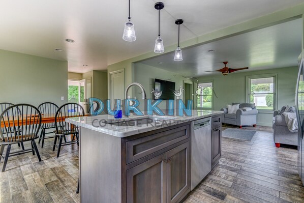 A modern kitchen with a central island, pendant lighting, and a dining area with chairs.
