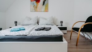 A modern bedroom with a large bed, two bedside tables, a chair, and a painting on the wall.
