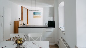 A compact kitchen with white cabinets, a wooden dining table with a floral tablecloth, and a small island with a microwave.