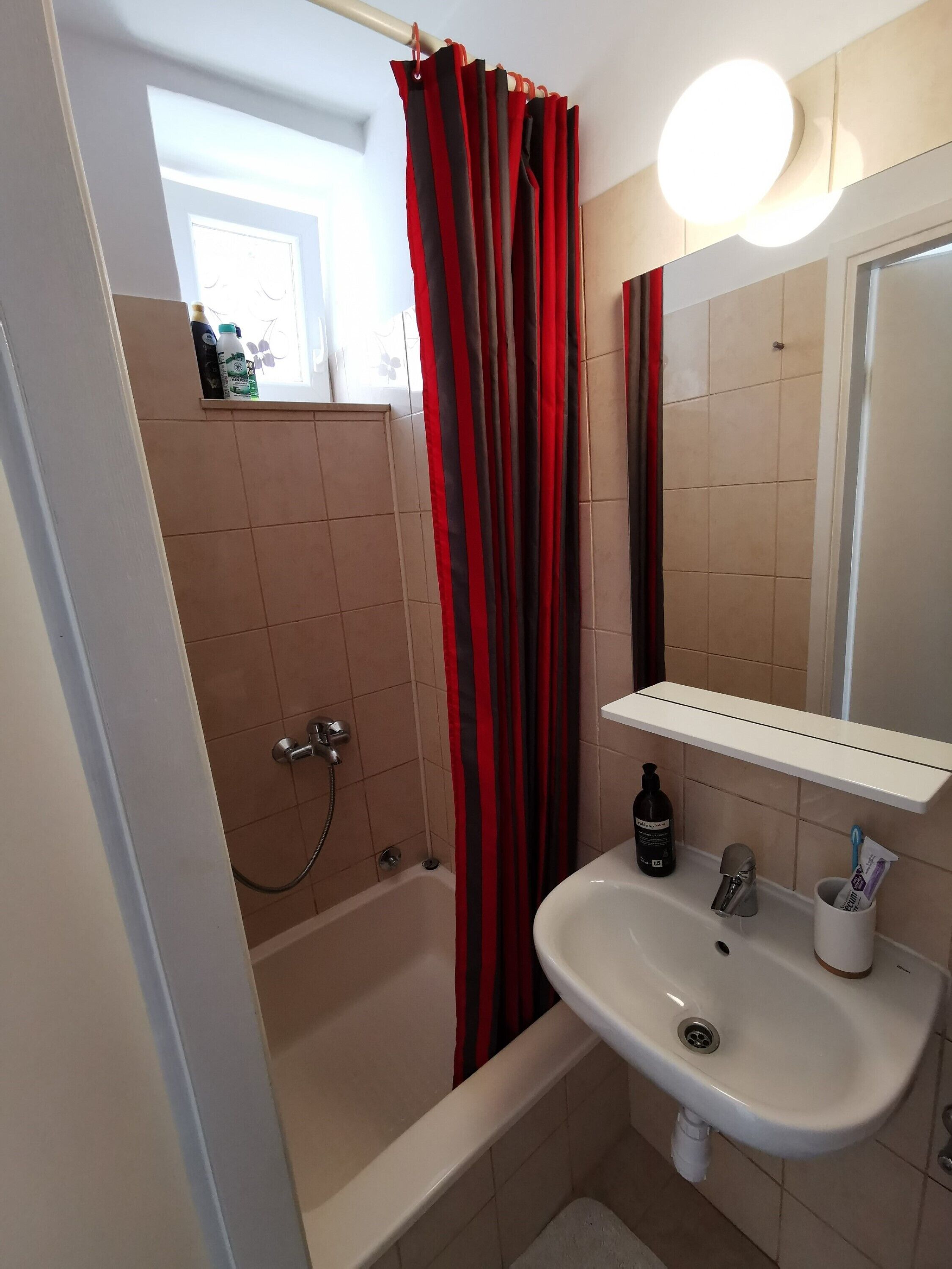 Un bany amb banyera, un lavabo, un mirall i una cortina de dutxa.