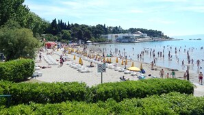 A beach with rows of sun loungers and umbrellas, a clear sky, and a calm sea.