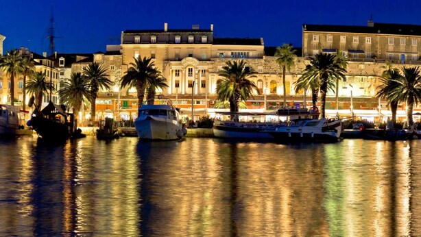 A waterfront with boats docked, historic buildings, and palm trees.