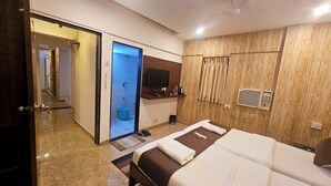 Quarto de hotel com uma cama grande, banheiro com chuveiro e uma pequena área de trabalho.