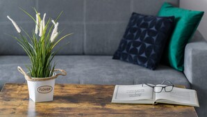 Una planta en maceta con una etiqueta sobre una mesa de madera, un libro y un par de gafas.