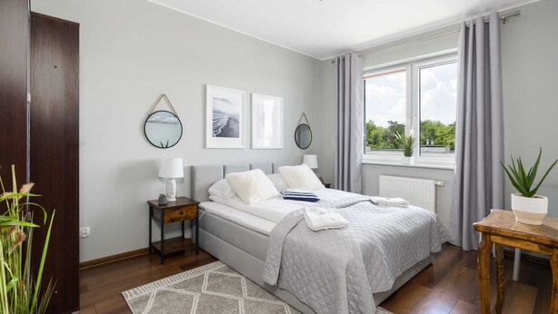 Un dormitorio con cama, mesitas de noche, una ventana con cortinas y vistas al exterior con vegetación.