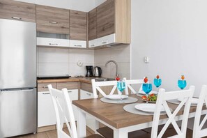 A modern kitchen with white cabinets, a stainless steel refrigerator, and a wooden dining table with white chairs.