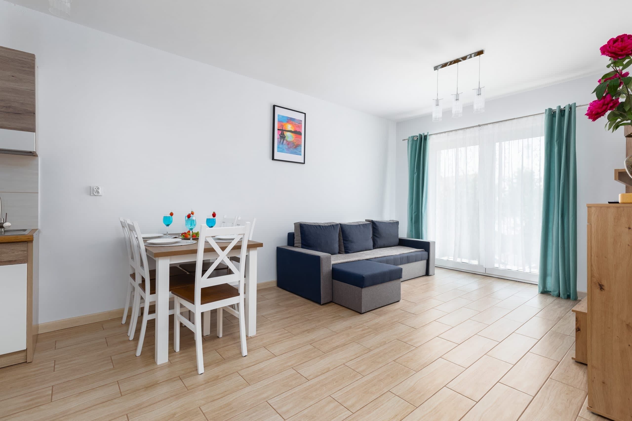 A modern living space with a dining area, sofa, and large windows with curtains.