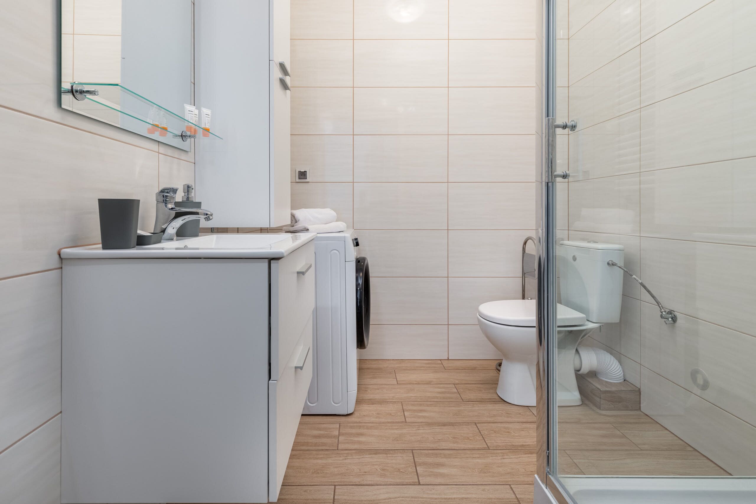 Une salle de bain moderne avec une douche à parois de verre, un lavabo blanc avec un miroir, des toilettes et un lave-linge.