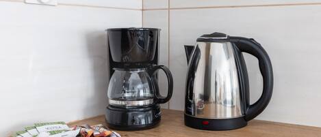 A coffee maker, a kettle, and a plate with coffee packets on a wooden table.