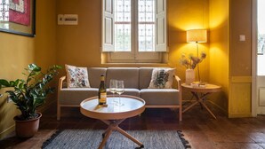 A room with a sofa, a round table with a bottle and glasses, a potted plant, a lamp, and a window with white shutters. - Villa "Masia Can Comas" with Pool, Garden & Wi-Fi (Torrelavit)