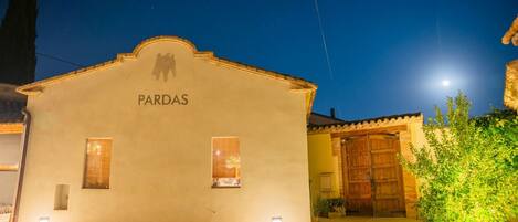 A building with the name 'PARDAS' at night, featuring a traditional facade, a wooden door, and a small garden area.