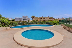 A swimming pool with a circular design, surrounded by a low stone wall and a metal fence.