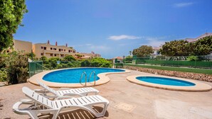 A pool area with two white lounge chairs, a pool with a curved edge, and a building in the background.