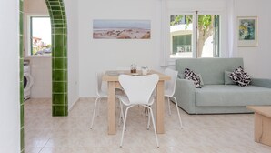 A room with a dining table, chairs, a sofa, a painting, and a view through a window.