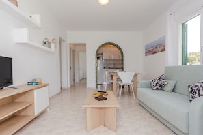 A modern living room with a TV, a wooden coffee table, a sofa, and a dining area with chairs.