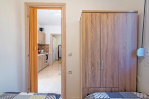 A bedroom with a bed, a wardrobe, and a view into a kitchen area.