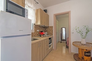 A kitchen with a refrigerator, microwave, and wooden cabinets. There is a sink and a countertop with a vase of flowers. A dining area with a table and chairs is visible in the background.