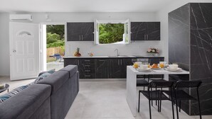A modern kitchen with a central island, black marble cabinets, and a view of greenery outside.