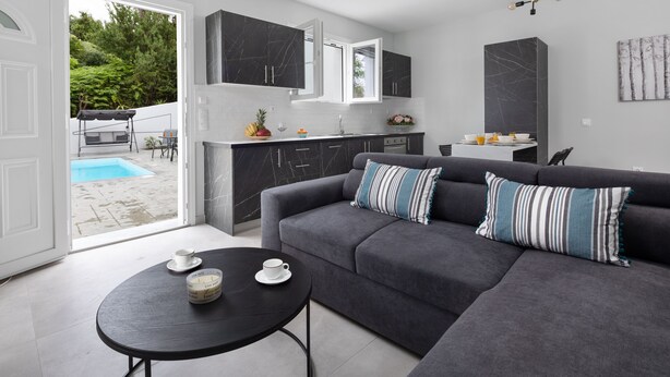 A modern kitchen with dark cabinets, a grey sofa with striped cushions, and a dining area with a table and chairs.