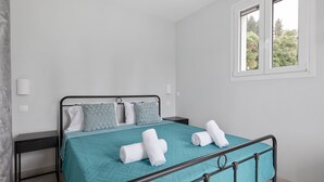 A bedroom with a teal bedspread, a metal bed frame, a nightstand, and a window with a view of trees.