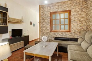 A living room with a stone wall, a television, a sofa, and a table. - Vacatio Home El Rinconcito del Faro with Sea View, Wi-Fi & Terrace (Gáldar)