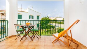 A balcony with a table and chairs, a wooden easel, and a view of a white building with green shutters. - Apartment "Los Delfines Biniforcat" with Private Covered Terrace and Shared Pool (Ciudadela)
