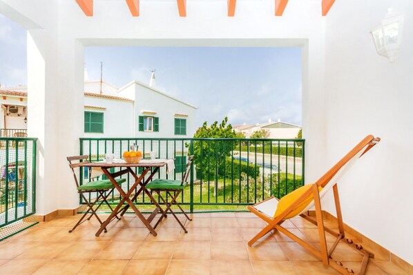 Un balcon avec une table et des chaises, un chevalet en bois et une vue sur un bâtiment blanc aux volets verts.