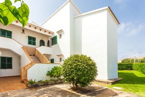 Un bâtiment blanc avec un escalier, un petit arbre et une pelouse bien entretenue.